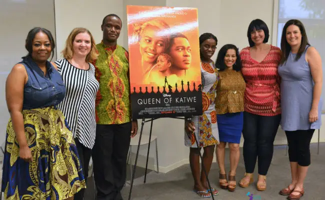 Robert Katende and Phiona Mutesi nexxt to a poster of the Queek of Katwe movie